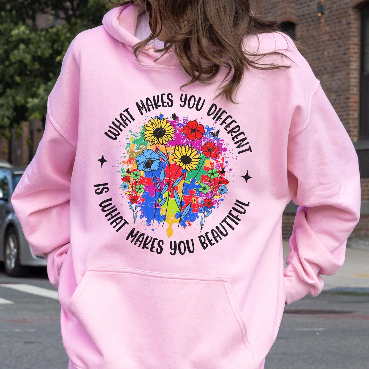 May include: A light pink hoodie with a front pocket and drawstring hood. The back features a colorful floral design with the text "WHAT MAKES YOU DIFFERENT IS WHAT MAKES YOU BEAUTIFUL" in a circular arrangement.