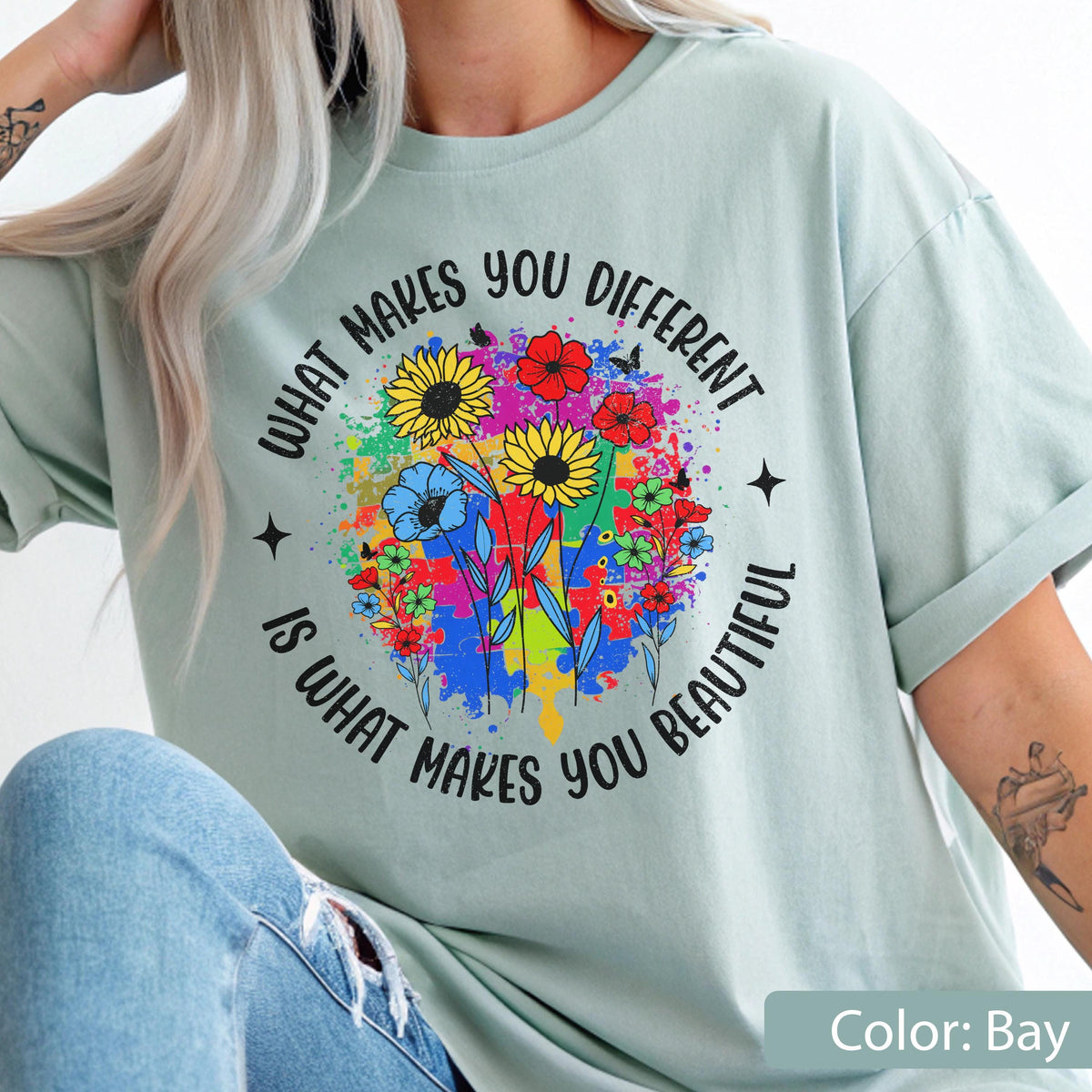 May include: A light green t-shirt with the text "WHAT MAKES YOU DIFFERENT IS WHAT MAKES YOU BEAUTIFUL" encircling a colorful floral design. The design includes sunflowers, other flowers, and a puzzle piece background.