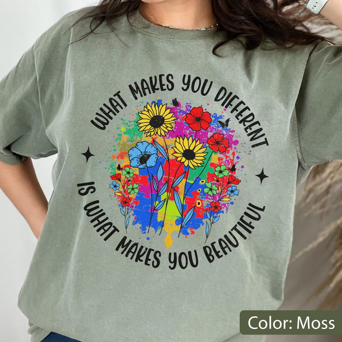 May include: Moss green t-shirt with a colorful floral design and the text "WHAT MAKES YOU DIFFERENT IS WHAT MAKES YOU BEAUTIFUL". The design features sunflowers, red and blue flowers, and a splash of colors.
