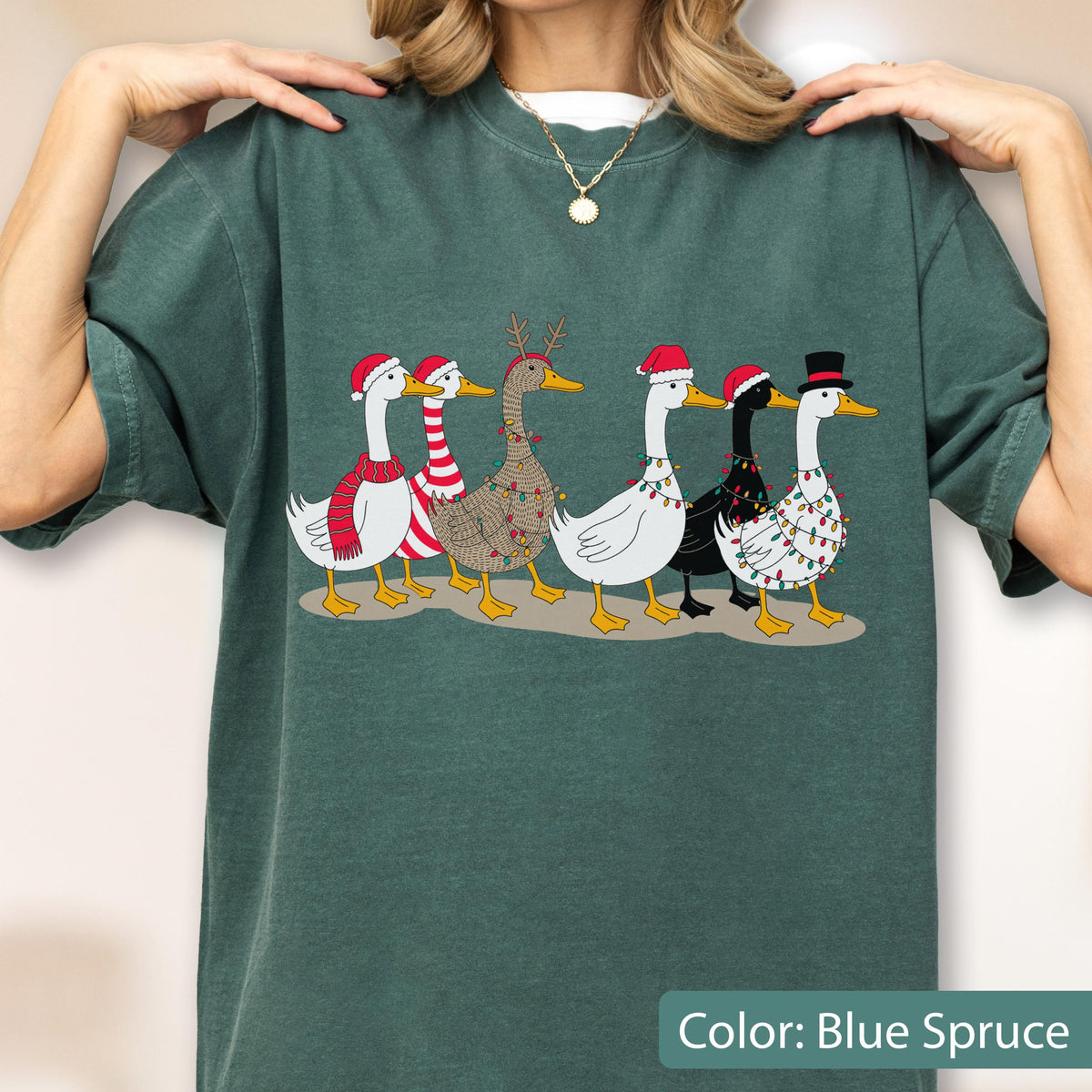 May include: A dark green t-shirt featuring a graphic of six geese walking in a line. The geese are decorated with Christmas elements including Santa hats, a top hat, a red and white striped scarf, reindeer antlers, and colorful string lights.