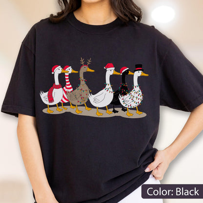 May include: A black short-sleeve t-shirt featuring a graphic print of six ducks in a row. The ducks are decorated with various holiday accessories including Santa hats, a top hat, a red and white striped scarf, reindeer antlers, and colorful string lights.