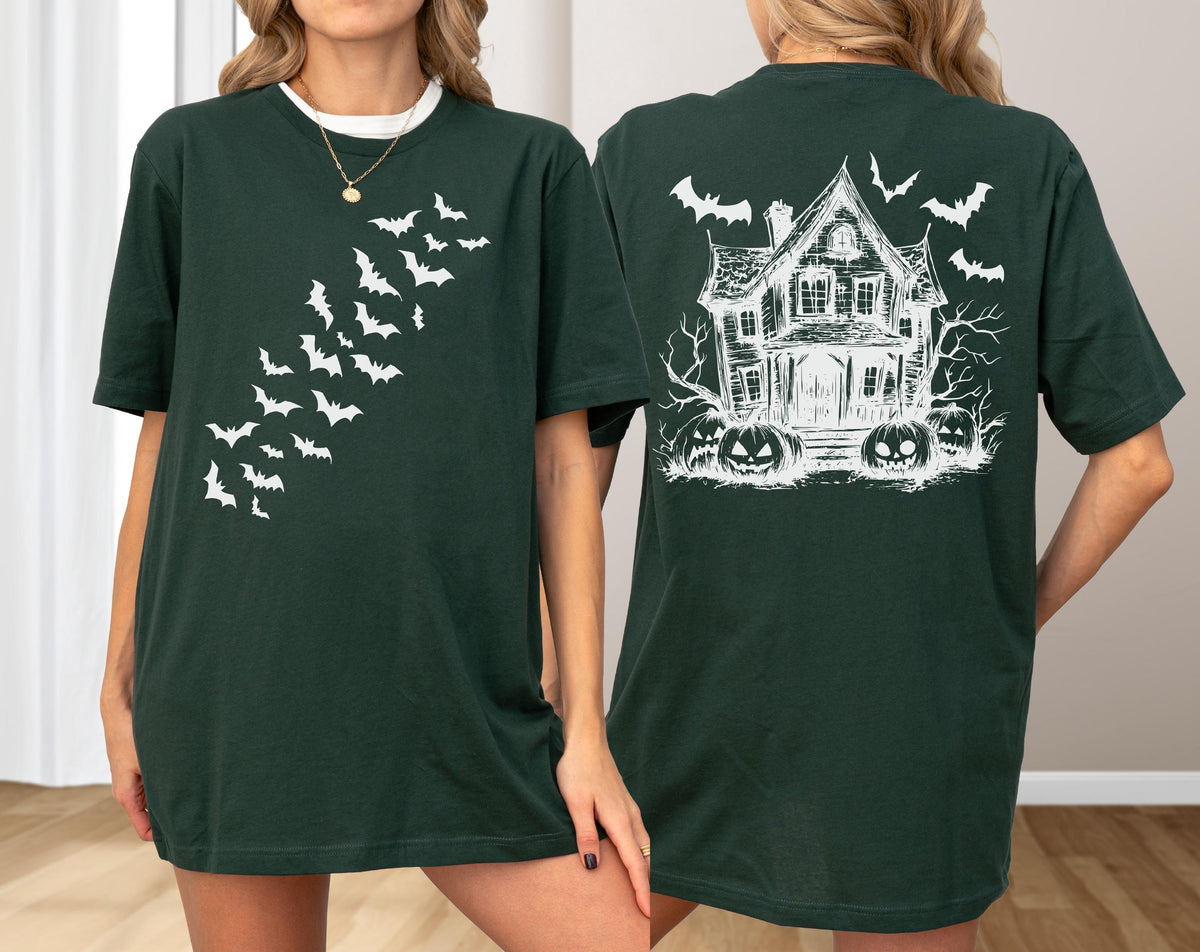May include: Dark green t-shirt featuring a white bat design on the front and a haunted house with bats and pumpkins on the back. The shirt has a crew neck and short sleeves. The design is a Halloween theme.