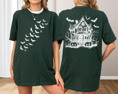 May include: Dark green t-shirt featuring a white bat design on the front and a haunted house with bats and pumpkins on the back. The shirt has a crew neck and short sleeves. The design is a Halloween theme.