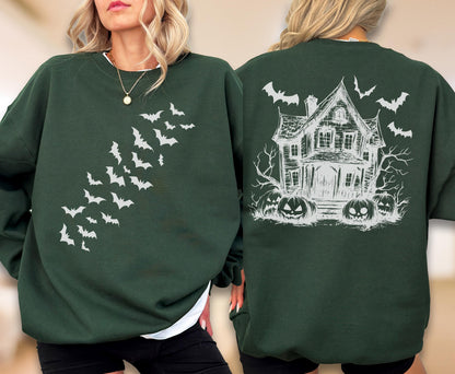 May include: A dark green crewneck sweatshirt featuring a white graphic print. The front displays a diagonal swarm of flying bats. The back showcases a detailed sketch of a haunted house surrounded by bare trees, jack-o'-lanterns, and flying bats.