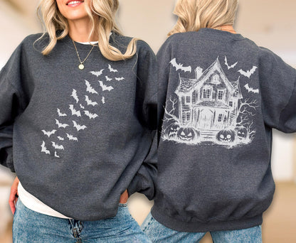 May include: A dark charcoal gray crewneck sweatshirt featuring a white graphic of a swarm of bats on the front. The back of the sweatshirt displays a detailed white sketch of a haunted house surrounded by bare trees, flying bats, and jack-o'-lanterns.