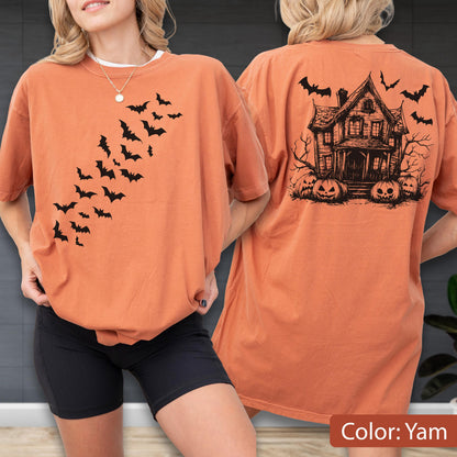 May include: An orange t-shirt featuring a black graphic of a swarm of bats on the front chest. The back of the shirt displays a detailed black illustration of a haunted house surrounded by bare trees and several carved jack-o'-lantern pumpkins.
