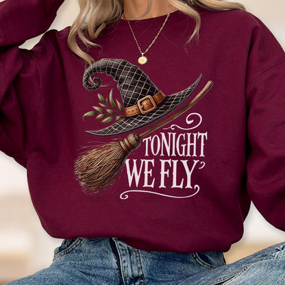 May include: A maroon long-sleeve sweatshirt featuring a graphic of a black witch hat with a brown buckle and green leaves, paired with a wooden broomstick. The text TONIGHT WE FLY is printed in white in a decorative serif font on the front.