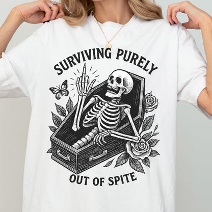 May include: A white t-shirt featuring a black graphic of a skeleton inside a coffin, giving the middle finger. The design includes roses, a butterfly, and the text "SURVIVING PURELY OUT OF SPITE" printed in a bold, arched black font above and below.