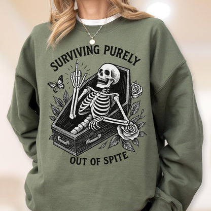 May include: Olive green sweatshirt with a graphic of a skeleton in a coffin, giving the middle finger. The text reads "SURVIVING PURELY" above and "OUT OF SPITE" below the graphic. A butterfly and roses are also featured.
