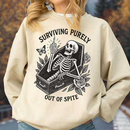 May include: Beige sweatshirt with a graphic of a skeleton in a coffin, giving the middle finger. The text reads "SURVIVING PURELY OUT OF SPITE". A butterfly and roses are also featured in the design.