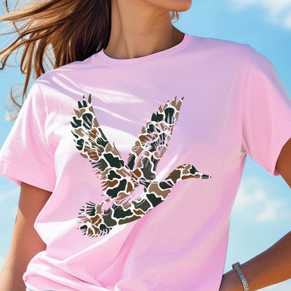 May include: A light pink short-sleeve t-shirt featuring a graphic of a flying duck. The duck is filled with a camouflage pattern consisting of brown, tan, dark green, and black organic shapes. The shirt has a crew neckline and a standard fit.