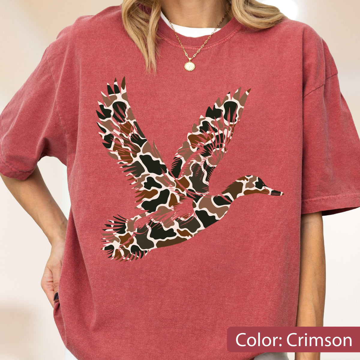 May include: A crimson short-sleeve t-shirt featuring a large graphic of a flying duck. The duck silhouette is filled with a brown, black, and white camouflage pattern. The shirt has a crew neckline and a relaxed fit, showcasing a bold animal design.