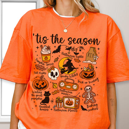 May include: Orange t-shirt with the phrase "'tis the season" and Halloween-themed graphics. The design includes a pumpkin spice latte, bats, a skull, a jack-o'-lantern, and other spooky elements. The shirt is a festive apparel item.