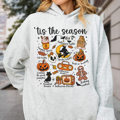 May include: A light gray hoodie featuring a colorful Halloween-themed graphic. The design includes pumpkins, bats, a witch, and the phrase "'tis the season." Other elements include "Pumpkin Spices" and "Trick or Treating."