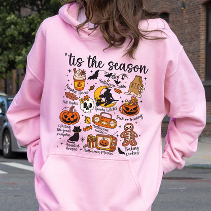 May include: Pink hoodie with a Halloween-themed graphic. The design includes a pumpkin, skull, bats, and the phrase "'tis the season." Other elements include "Pumpkin Spices," "Halloween Lights," and "Trick or Treating."