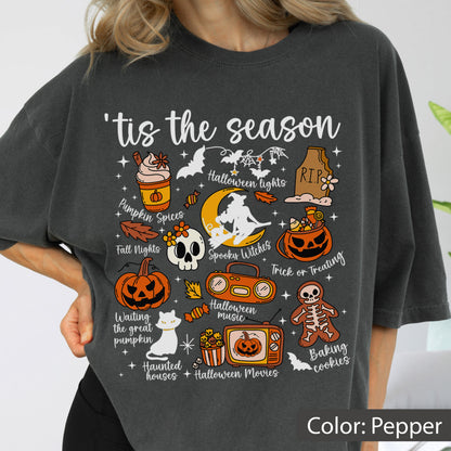 May include: A charcoal gray t-shirt featuring a graphic print with the text 'tis the season and various Halloween-themed illustrations including a pumpkin spice drink, a skull, a witch on a moon, a jack-o'-lantern, a cat, and a skeleton cookie.