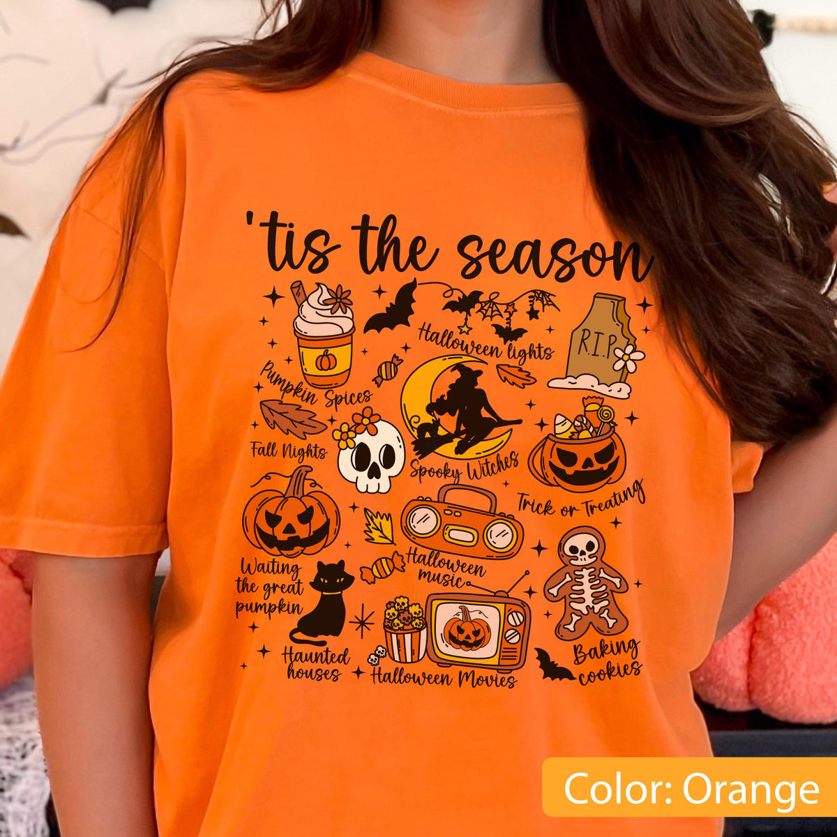 May include: An orange t-shirt featuring a black graphic print with the text 'tis the season' and various Halloween-themed illustrations including a pumpkin spice drink, a witch on a moon, a skull, a jack-o'-lantern, a black cat, and a skeleton cookie.