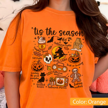 May include: An orange t-shirt featuring a black graphic print with the text 'tis the season' and various Halloween-themed illustrations including a pumpkin spice drink, a witch on a moon, a skull, a jack-o'-lantern, a black cat, and a skeleton cookie.