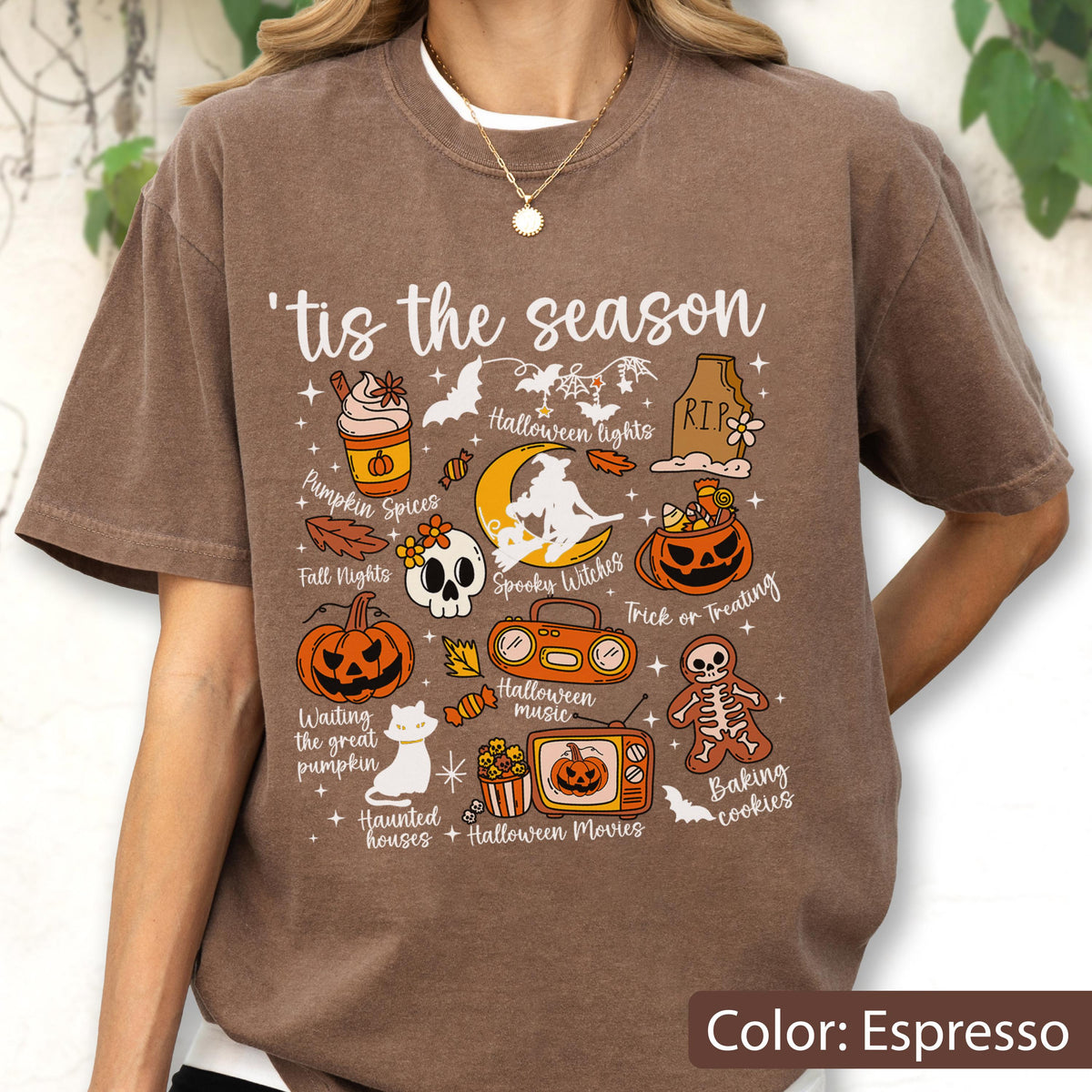 May include: An espresso-colored t-shirt featuring the text 'tis the season and various Halloween-themed illustrations including a pumpkin spice drink, a skull, a witch on a moon, a jack-o'-lantern, a boombox, a television, and a skeleton cookie.