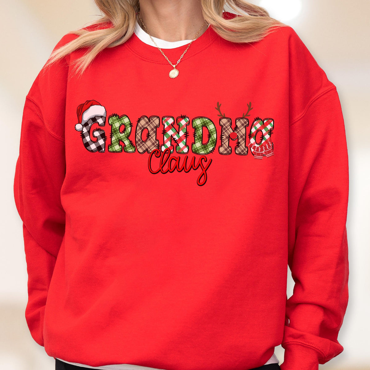 May include: A red sweatshirt with the words "Grandma Claus" in a festive design. The letters are decorated with plaid patterns, a Santa hat, and reindeer antlers, perfect for the holiday season.