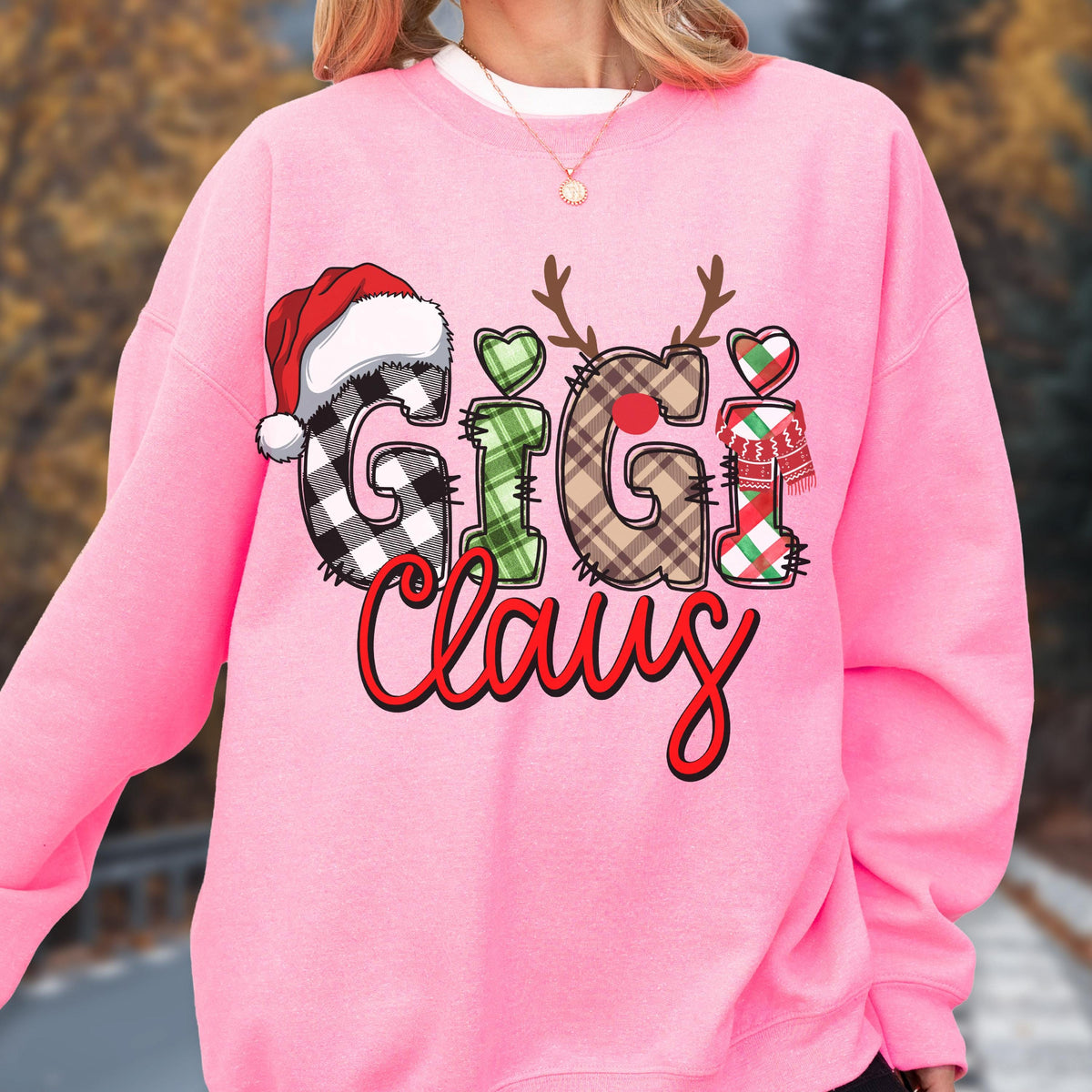 May include: A pink sweatshirt with the text "Gigi Claus" in a festive design. The letters are decorated with a Santa hat, reindeer antlers, hearts, and a scarf. The letters have plaid and green patterns.