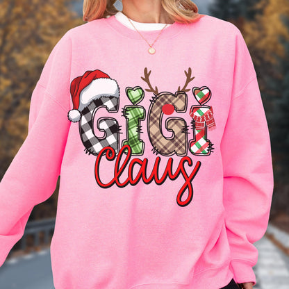 May include: A pink sweatshirt with the text "Gigi Claus" in a festive design. The letters are decorated with a Santa hat, reindeer antlers, hearts, and a scarf. The letters have plaid and green patterns.