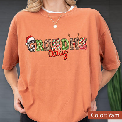 May include: A yam-colored short-sleeve t-shirt featuring the text "GRANDMA Claus" in a decorative font. The letters are filled with various plaid patterns in red, green, and brown, with a Santa hat on the G and reindeer antlers on the U.