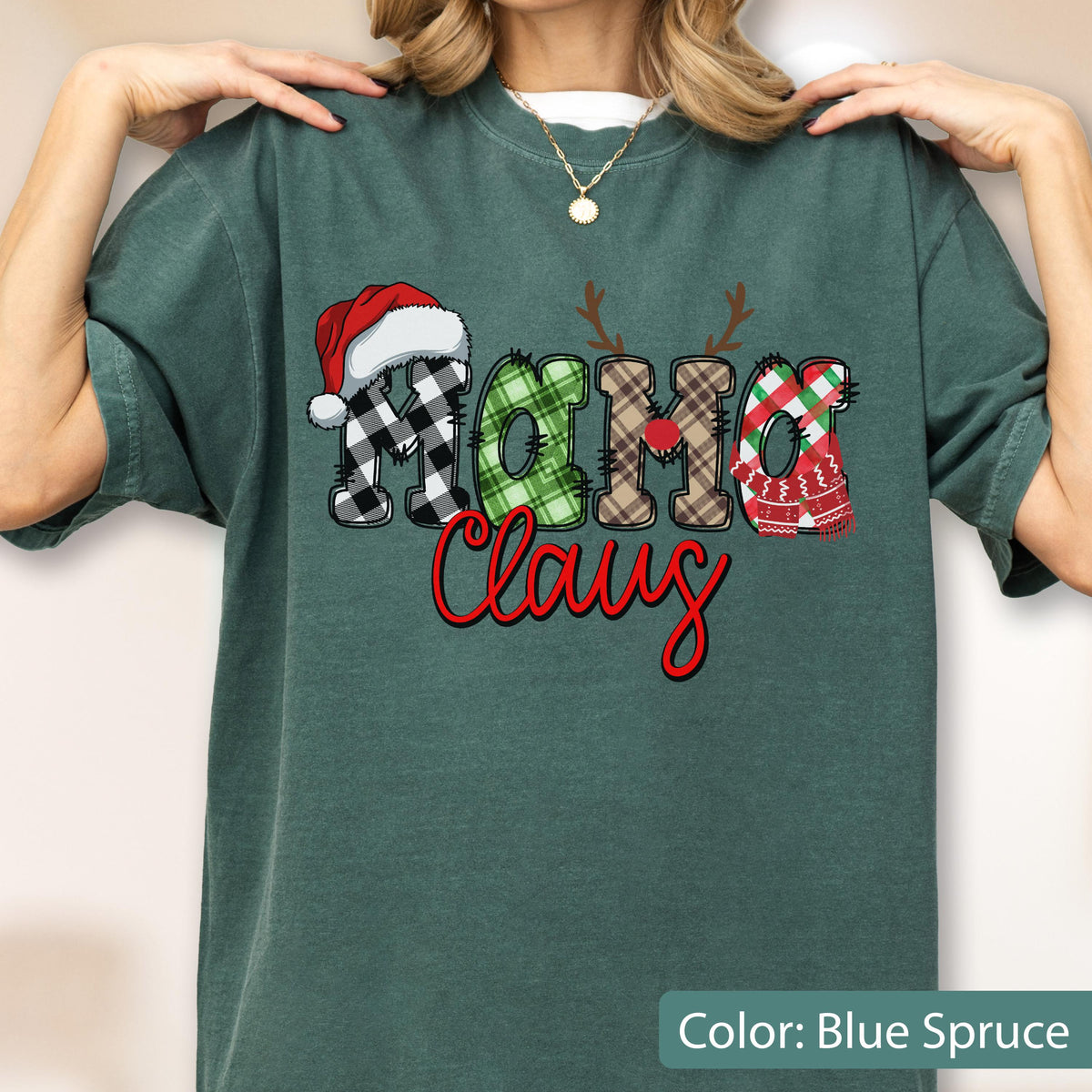 May include: A blue spruce t-shirt featuring the text "MAMA Claus" in a decorative font. The letters are filled with various plaid patterns, including black and white, green, and brown. A red Santa hat and reindeer antlers are on the letters.