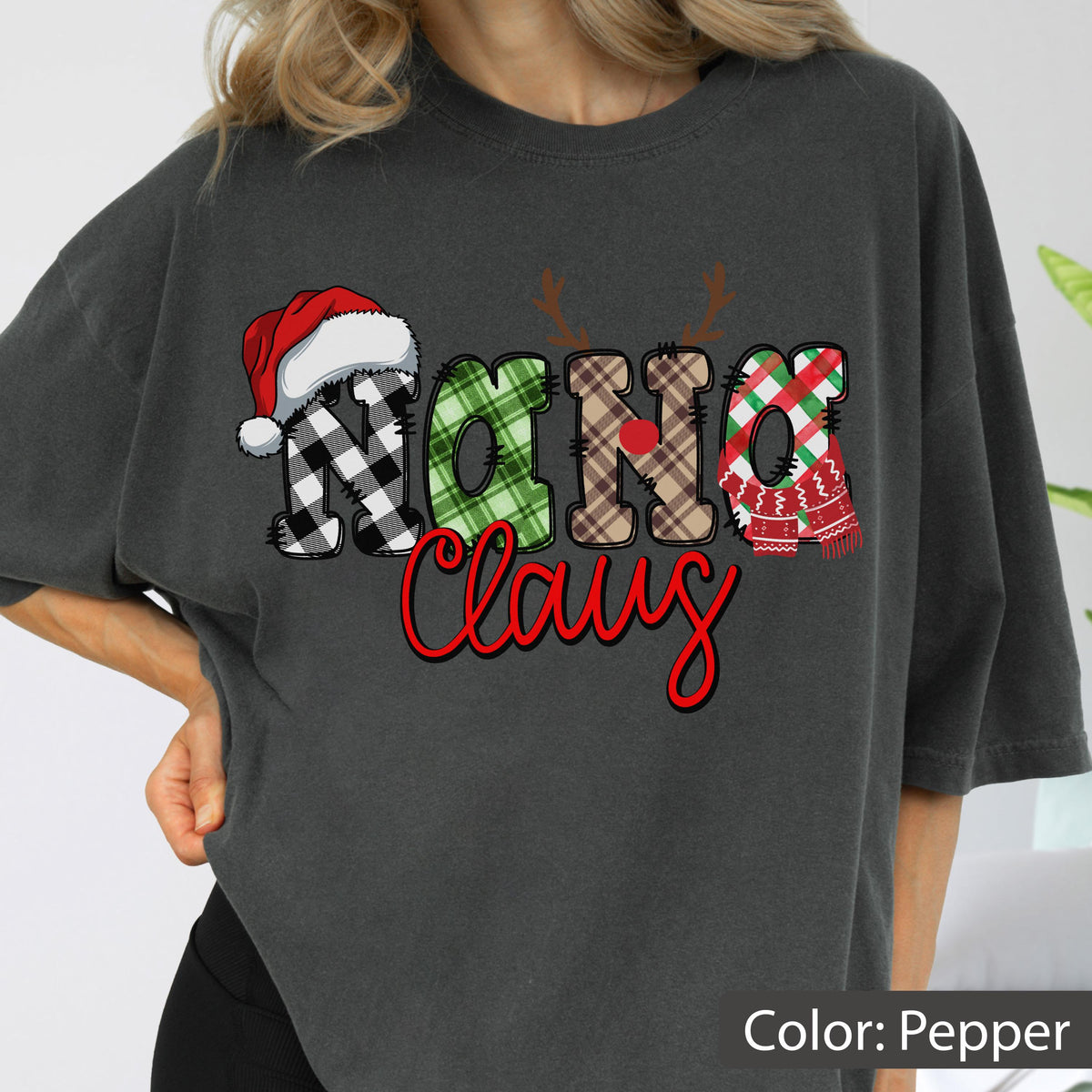 May include: A pepper-colored t-shirt featuring the text Nana Claus in a decorative font. The word Nana is styled with plaid patterns, a red Santa hat, reindeer antlers, and a red nose. The word Claus is written in a bold red script font.
