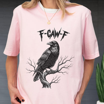 May include: A light pink t-shirt featuring a black and white illustration of a raven perched on a tree branch. The text "F-CAW-F" is above the raven. The shirt has short sleeves and a crew neck.