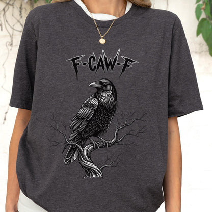 May include: Dark gray t-shirt featuring a detailed black raven perched on a branch. The shirt has the text "F-CAW-F" above the raven. The raven is intricately illustrated with a gothic aesthetic.