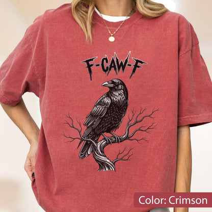 May include: A crimson short-sleeve t-shirt featuring a graphic of a black raven perched on a bare tree branch. Above the bird, the text F-CAW-F is printed in a sharp, jagged black font. The shirt has a crew neckline and a relaxed fit.