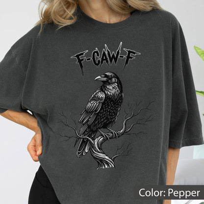 May include: A charcoal gray t-shirt featuring a graphic print of a black raven perched on a bare, twisted tree branch. Above the bird, the text F-CAW-F is printed in a jagged, stylized font. The shirt has a relaxed fit and short sleeves.