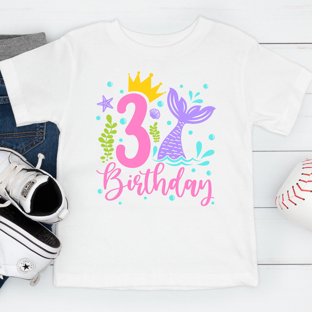 May include: White t-shirt with a colorful mermaid-themed design for a third birthday. The design includes a pink number 3, a mermaid tail, a crown, and the word "Birthday" in pink script.