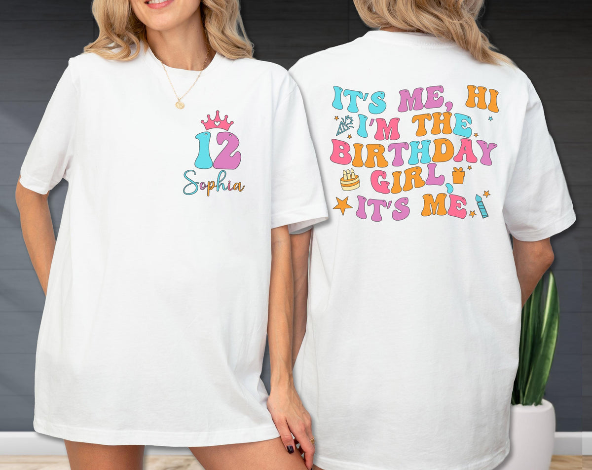 May include: White t-shirt with a colorful design. The front features a crown, the number 12 in blue and pink, and the name "Sophia". The back of the shirt says "It's me, hi I'm the birthday girl it's me" in retro colors.