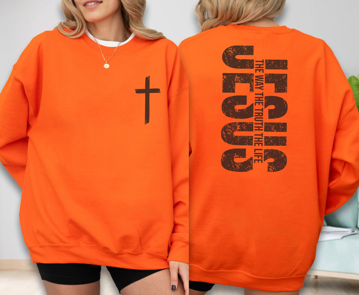 May include: Bright orange sweatshirt with a black cross on the front. The back of the sweatshirt features the word "JESUS" in large, distressed brown letters, with "THE WAY THE TRUTH THE LIFE" printed vertically.