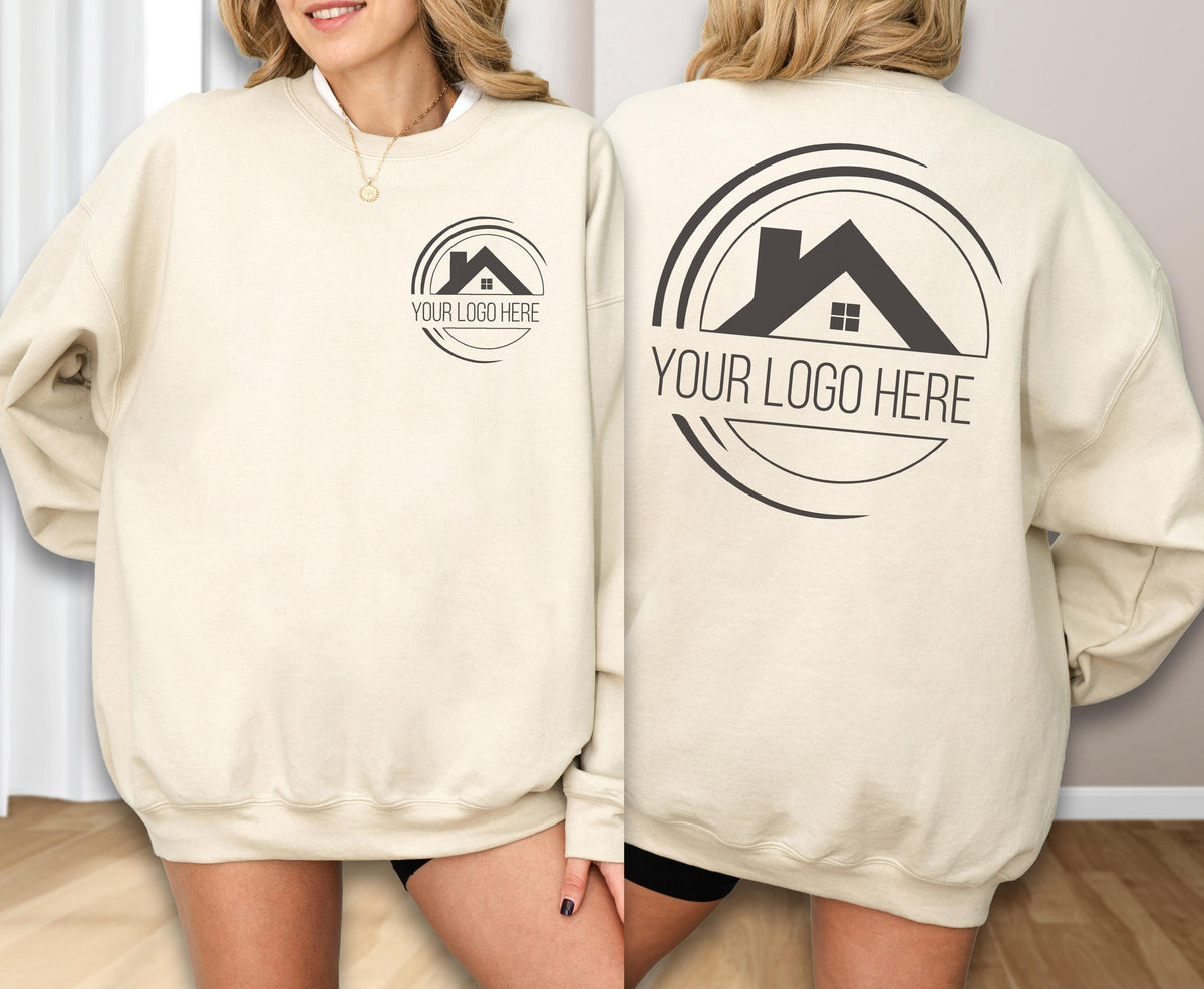 May include: Cream-colored sweatshirt with a circular logo featuring a house silhouette and the text "YOUR LOGO HERE". The logo is printed in black on both the front and back of the sweatshirt. The sweatshirt has a crew neck and long sleeves.