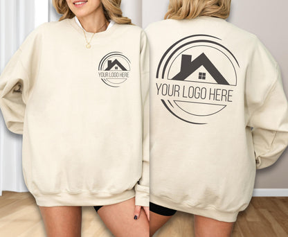 May include: Cream-colored sweatshirt with a circular logo featuring a house silhouette and the text "YOUR LOGO HERE". The logo is printed in black on both the front and back of the sweatshirt. The sweatshirt has a crew neck and long sleeves.