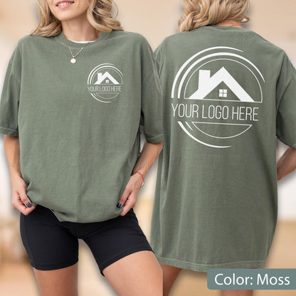May include: A moss-colored t-shirt with a white logo on the front and back. The logo features a house silhouette within a circular design, with the text "YOUR LOGO HERE" below. The shirt is short-sleeved and has a relaxed fit.