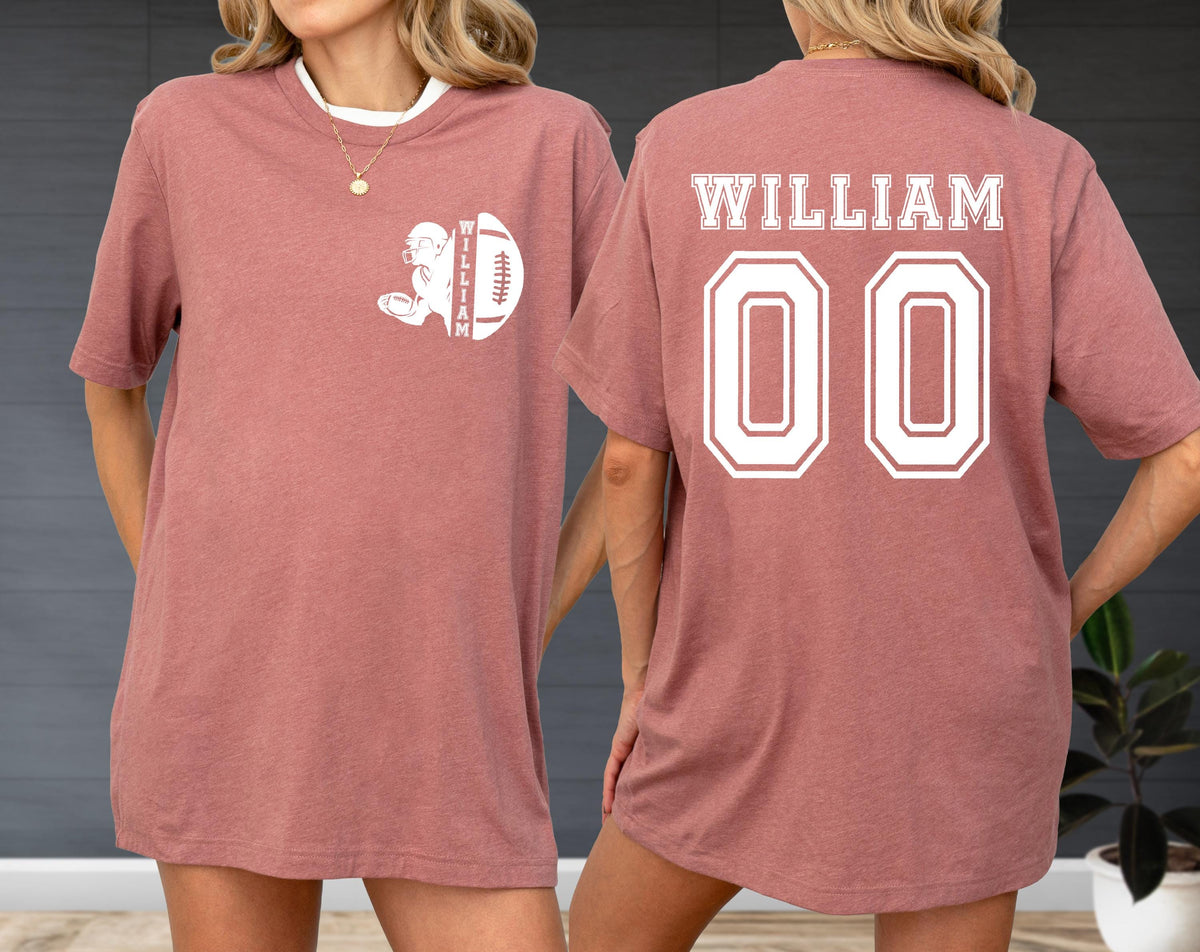 May include: A dusty rose t-shirt with a white collar. The front features a football graphic with the name "WILLIAM". The back displays "WILLIAM" above the number "00" in white block lettering. The shirt has short sleeves.