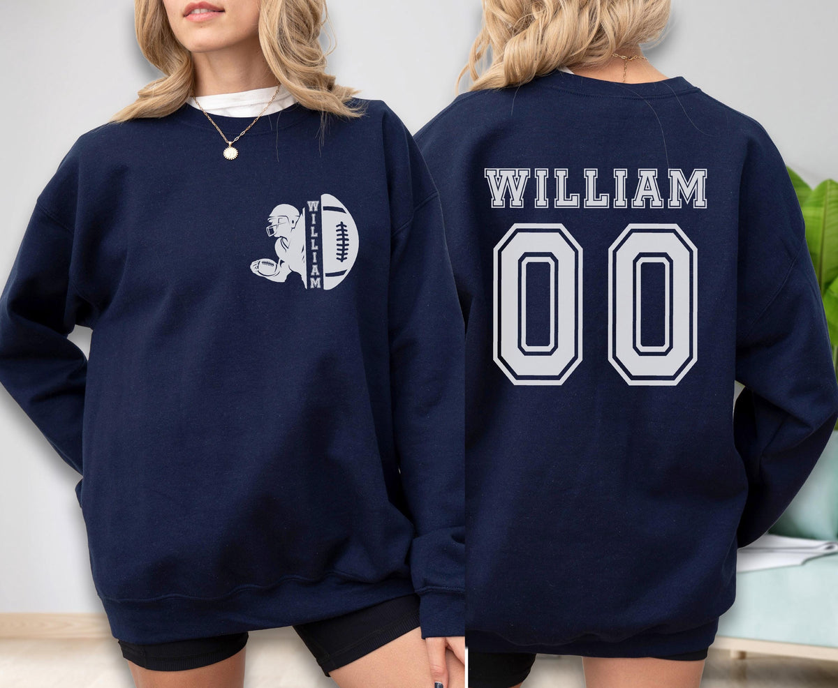 May include: A navy blue long-sleeve sweatshirt featuring a white graphic on the front left chest of a football player silhouette with the name WILLIAM and a football. The back displays the name WILLIAM in white text above the large number 00.