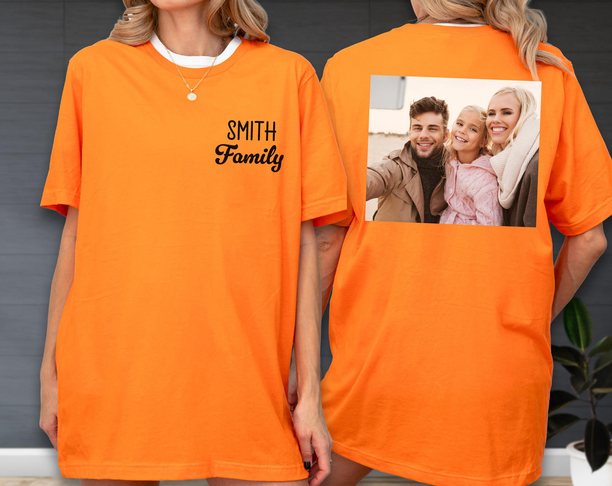 May include: Orange t-shirt with a white collar and the text "SMITH Family" in black script on the front. The back of the shirt features a color photograph of a family taking a selfie.