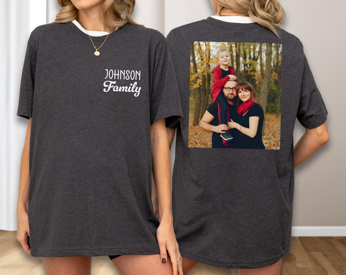 May include: Dark gray t-shirt with a white collar and the text "Johnson Family" on the front. The back of the shirt features a family photo in a square frame. The photo shows a family of three in a forest setting.