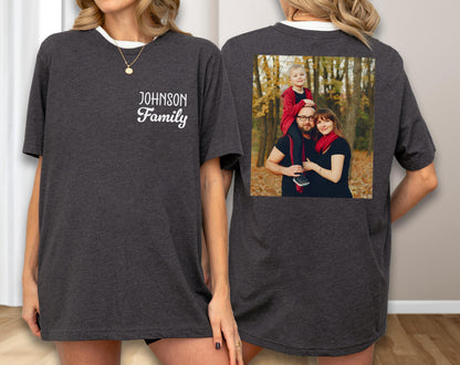 May include: Dark gray t-shirt with a white collar and the text "Johnson Family" on the front. The back of the shirt features a family photo in a square frame. The photo shows a family of three in a forest setting.