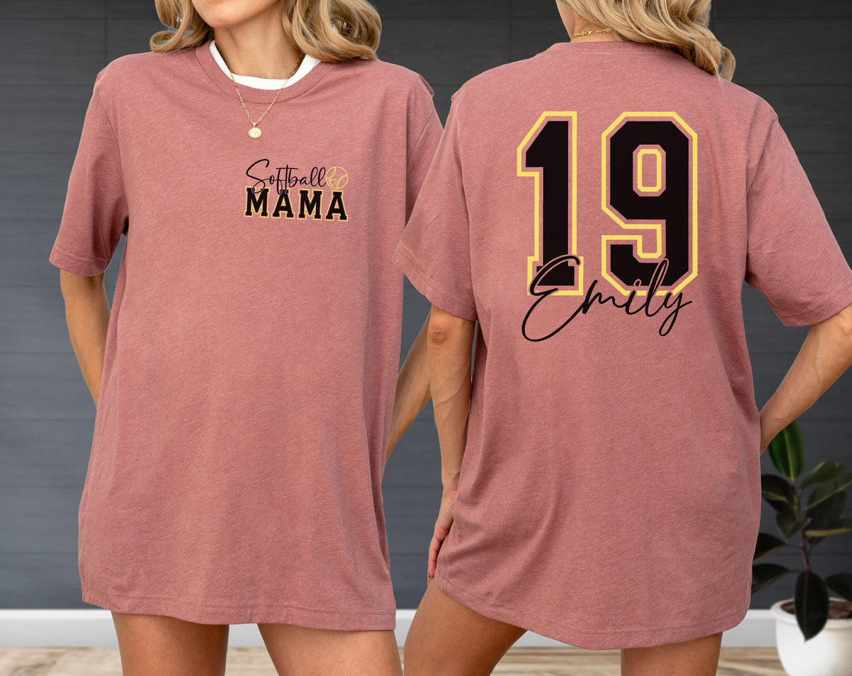 May include: Dusty rose t-shirt with "Softball Mama" text and a softball graphic on the front. The back features the number 19 in black and gold with the name "Emily" in script. The shirt has a crew neck and short sleeves.