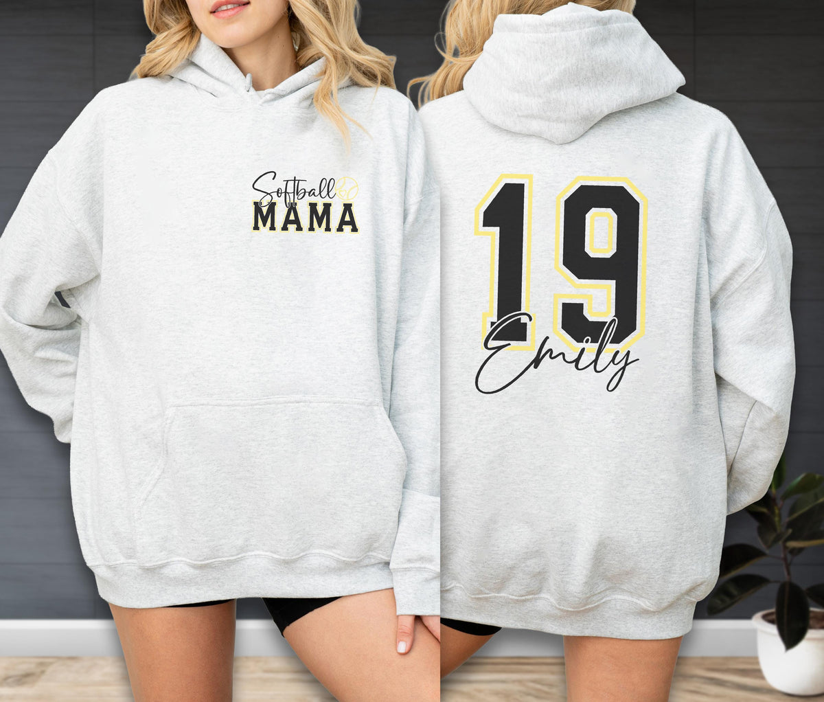 May include: Light gray hoodie with a front pocket and drawstring hood. The front features the text "Softball MAMA" in black and gold. The back displays the number "19" in black with a gold outline, and the name "Emily" in script.