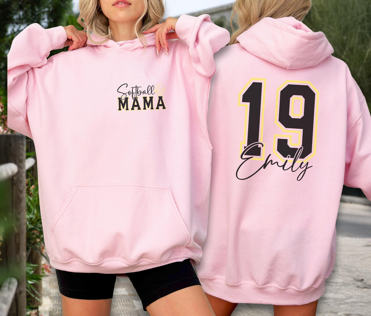 May include: A light pink hoodie with the text "Softball MAMA" on the front. The back of the hoodie features the number "19" in black with a yellow outline, and the name "Emily" in a script font. The hoodie has a front pocket and a hood.