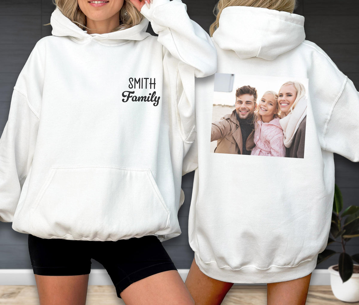 May include: White hoodie with a front pocket and hood. The front of the hoodie has the text "Smith Family" in a script font. The back of the hoodie features a family photo. The hoodie is worn by a person.