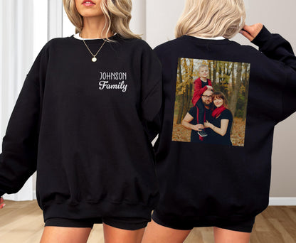 May include: Black sweatshirt with a white collar and the text "Johnson Family" embroidered on the front. The back of the sweatshirt features a family photo. The sweatshirt is a casual, comfortable garment.