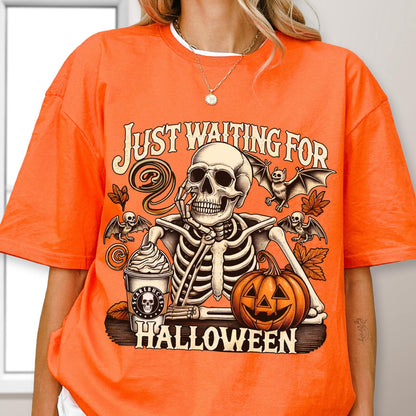 May include: Orange t-shirt with a Halloween-themed graphic. The design features a skeleton, bats, a pumpkin, and the text "JUST WAITING FOR HALLOWEEN". The skeleton is holding its chin, and a coffee cup is next to it.